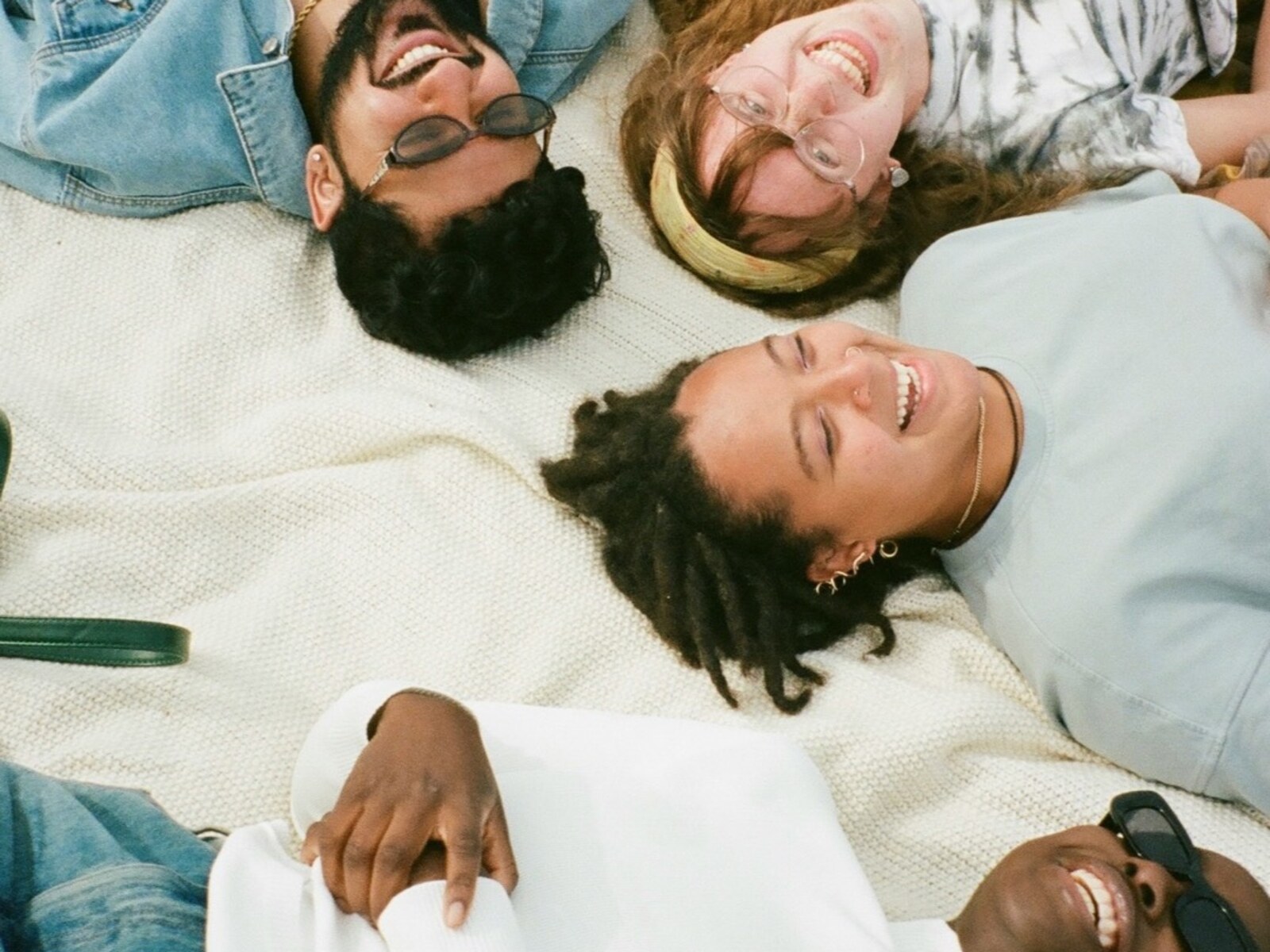 Four friends laughing together while relaxing on a blanket outdoors